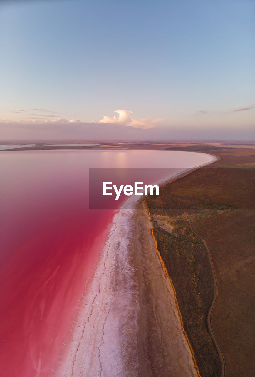 Panorama aerial view of pink salt lake in sunset light with clouds on horizon