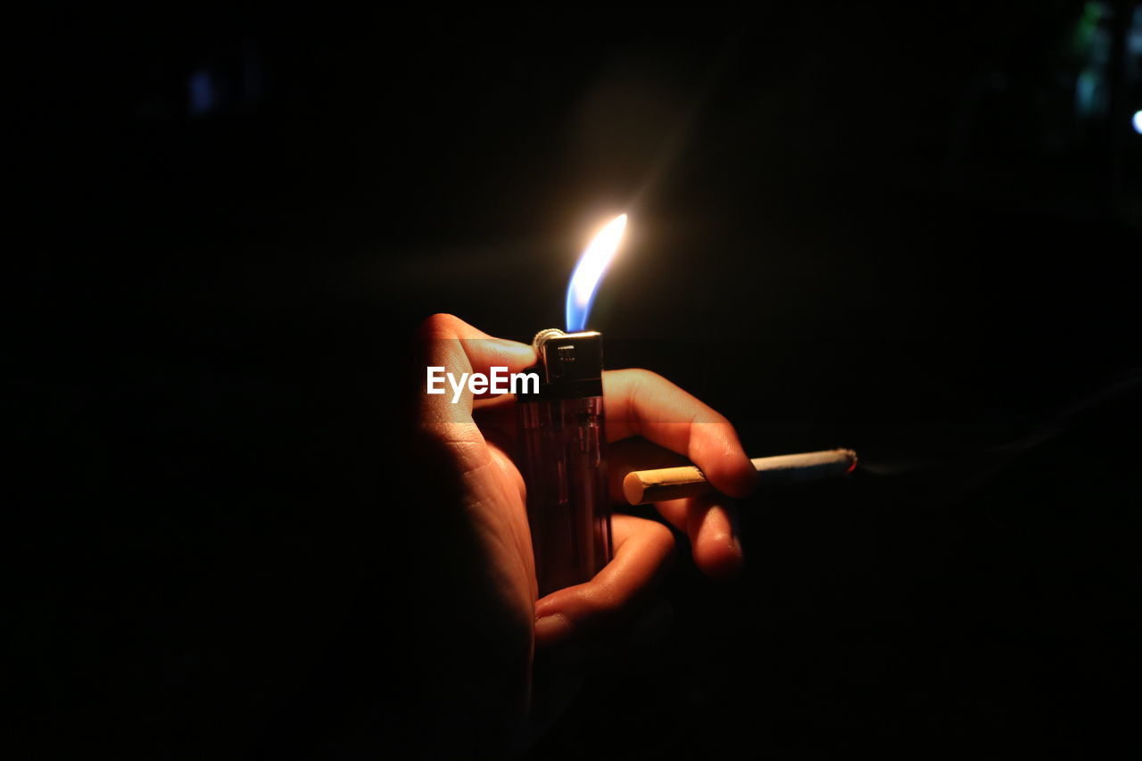 Close-up of human hand holding lighter and cigarette at night