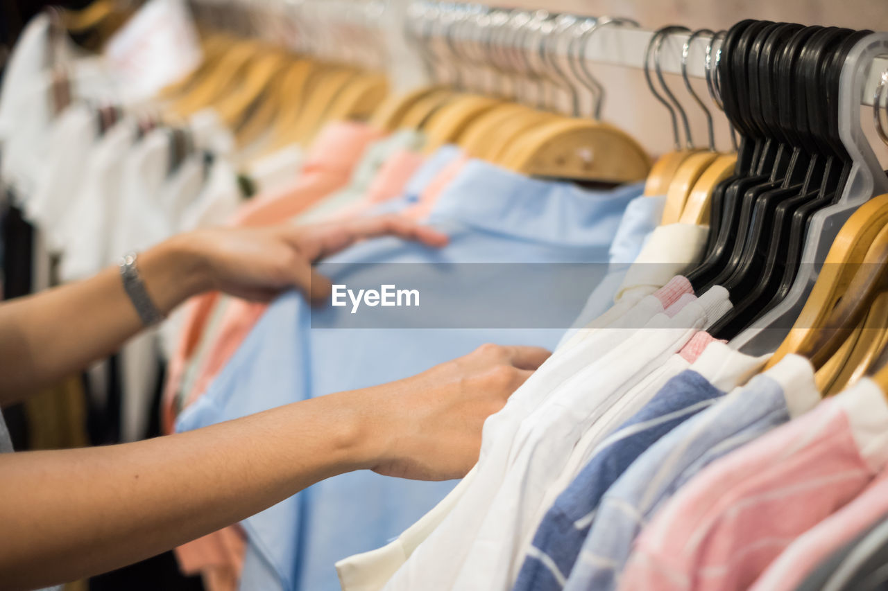 Cropped hands of woman choosing tops in clothing store