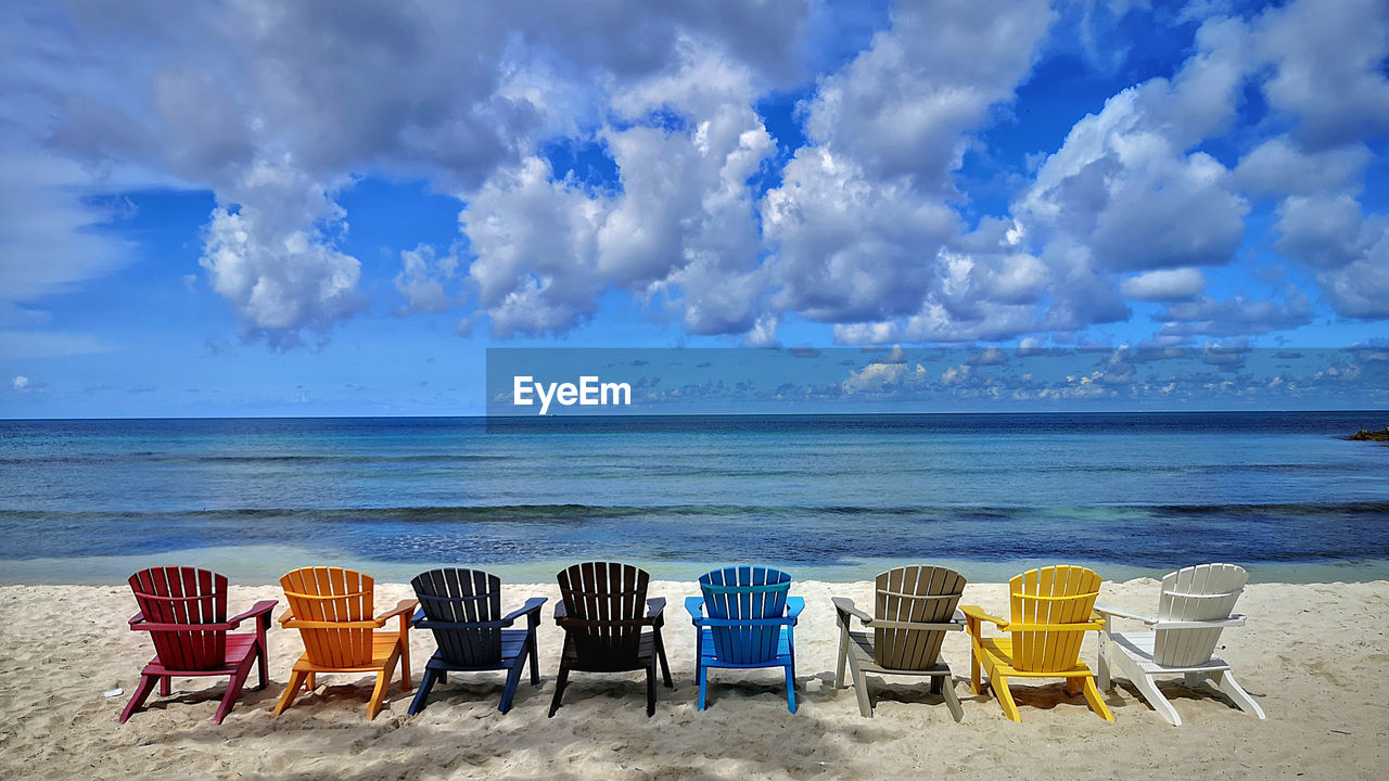 DECK CHAIRS ON BEACH AGAINST SKY