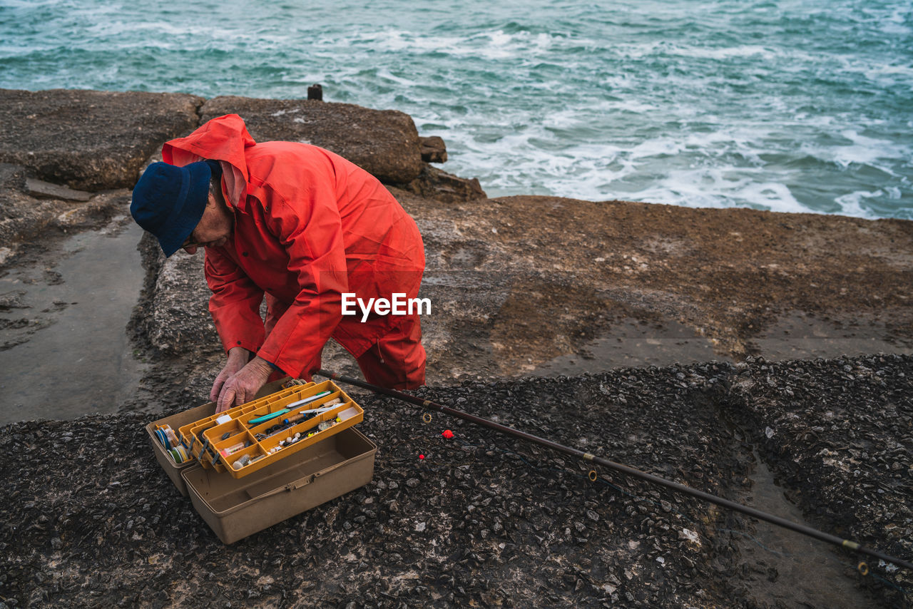 Man searching for fishing bait in container while standing by sea