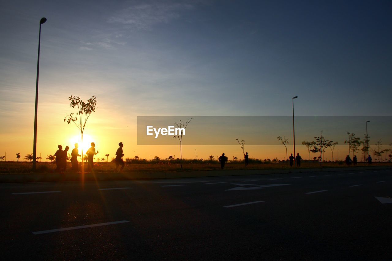 Silhouette people jogging on sidewalk against sunset sky