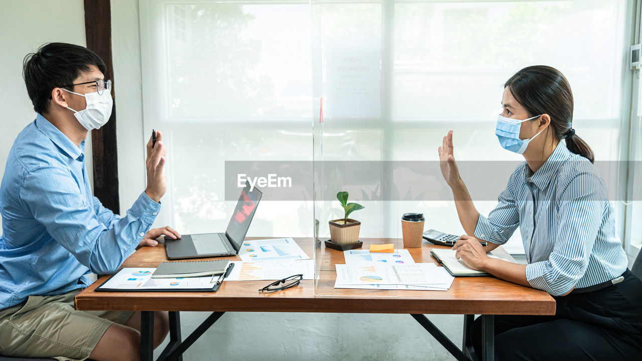 Male and female entrepreneur discussing through glass shield at office