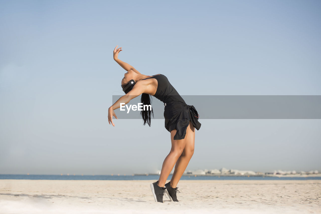 Young woman dancing at beach against clear sky