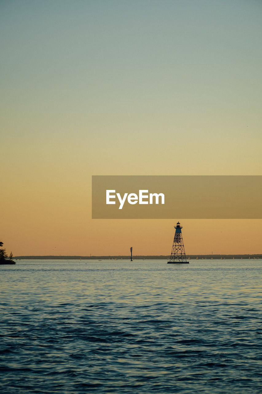 SILHOUETTE LIGHTHOUSE IN SEA AGAINST CLEAR SKY