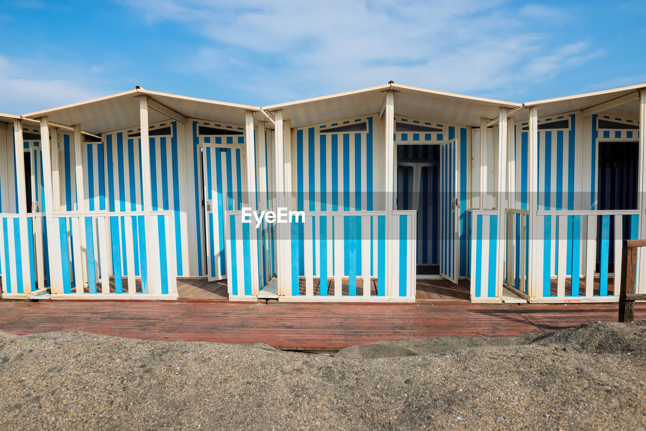 Striped white and blue striped beach houses and black sandy beach, tyrrhenian sea near roma, italy