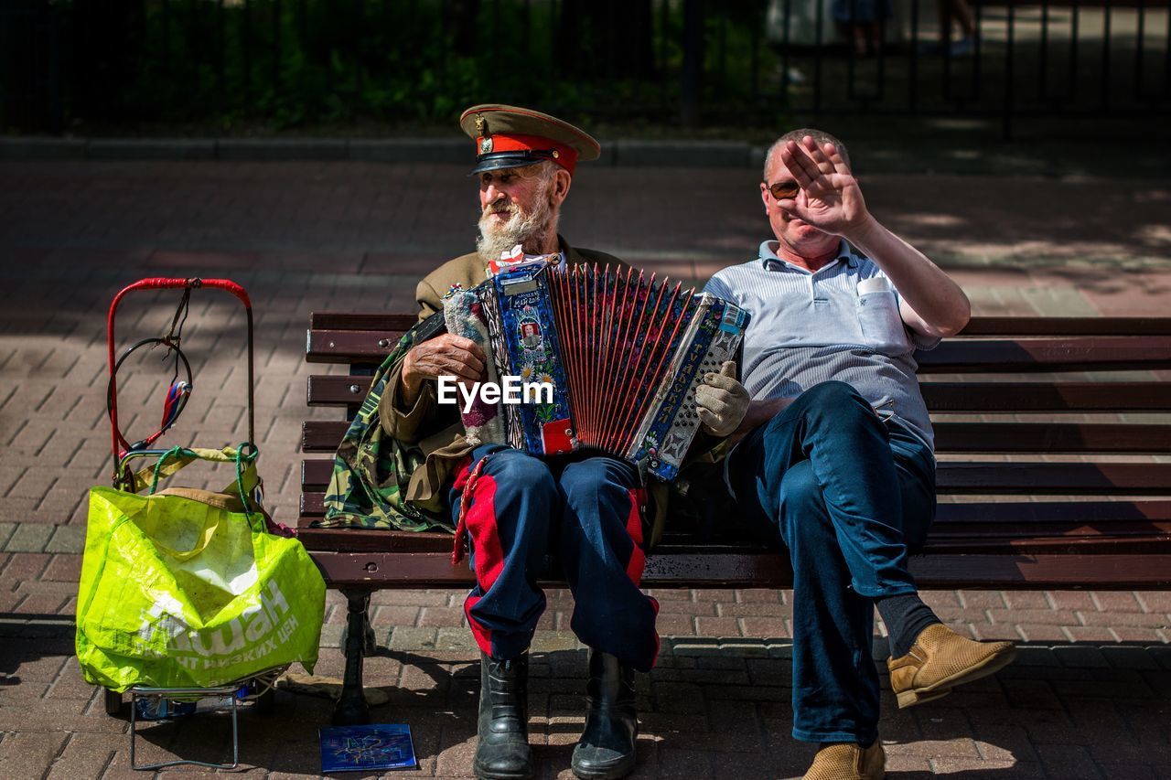 Full length of man sitting by street performer on bench