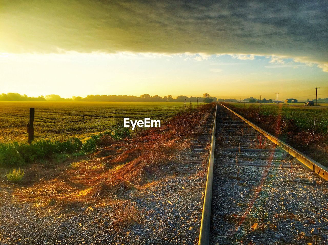 Railroad track on grassy field against cloudy sky at morning