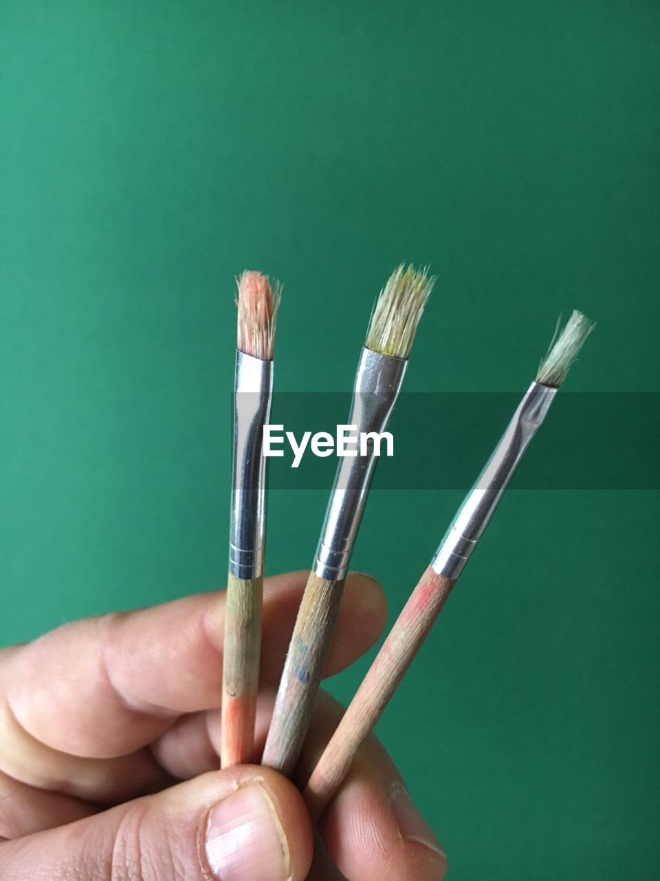 Cropped image of hand holding paintbrushes against green background