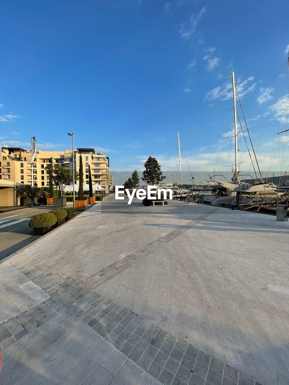 sky, architecture, transportation, city, built structure, building exterior, walkway, nature, cloud, mode of transportation, water, building, no people, blue, street, sea, day, travel destinations, ship, travel, coast, outdoors, vehicle, road, dock, nautical vessel, marina, harbor, urban area, tree, sunlight