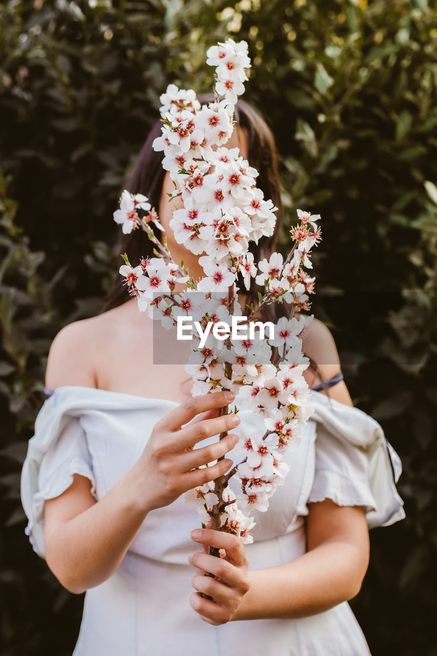 Woman holding flowers while standing against trees