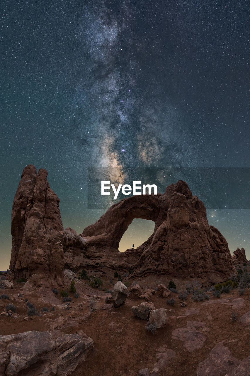 Unrecognizable traveler admiring breathtaking view of turret arch located near rough canyon against glowing milky way at night sky in arches national park in utah, usa