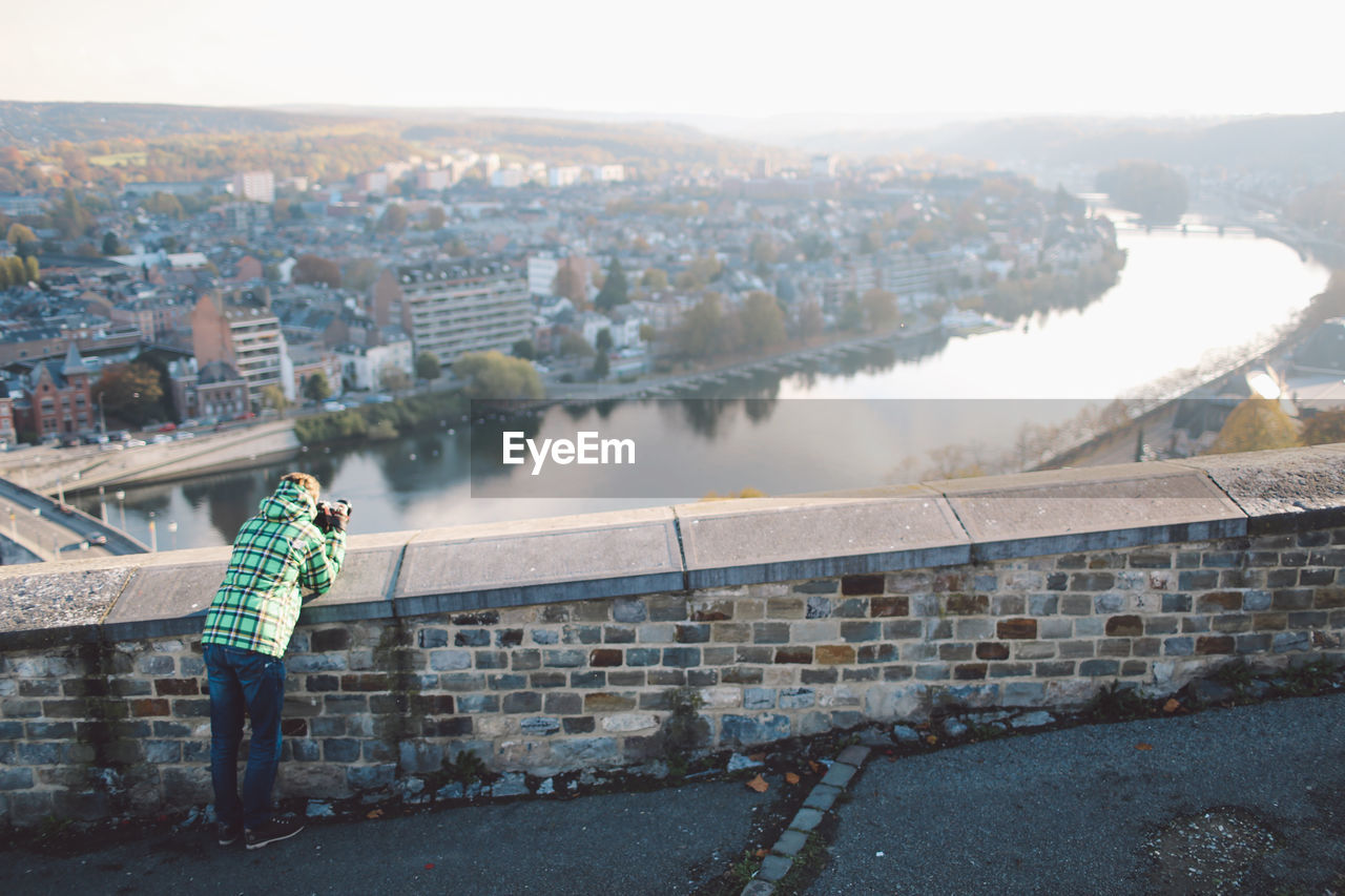 Rear view of woman photographing river amidst buildings in city