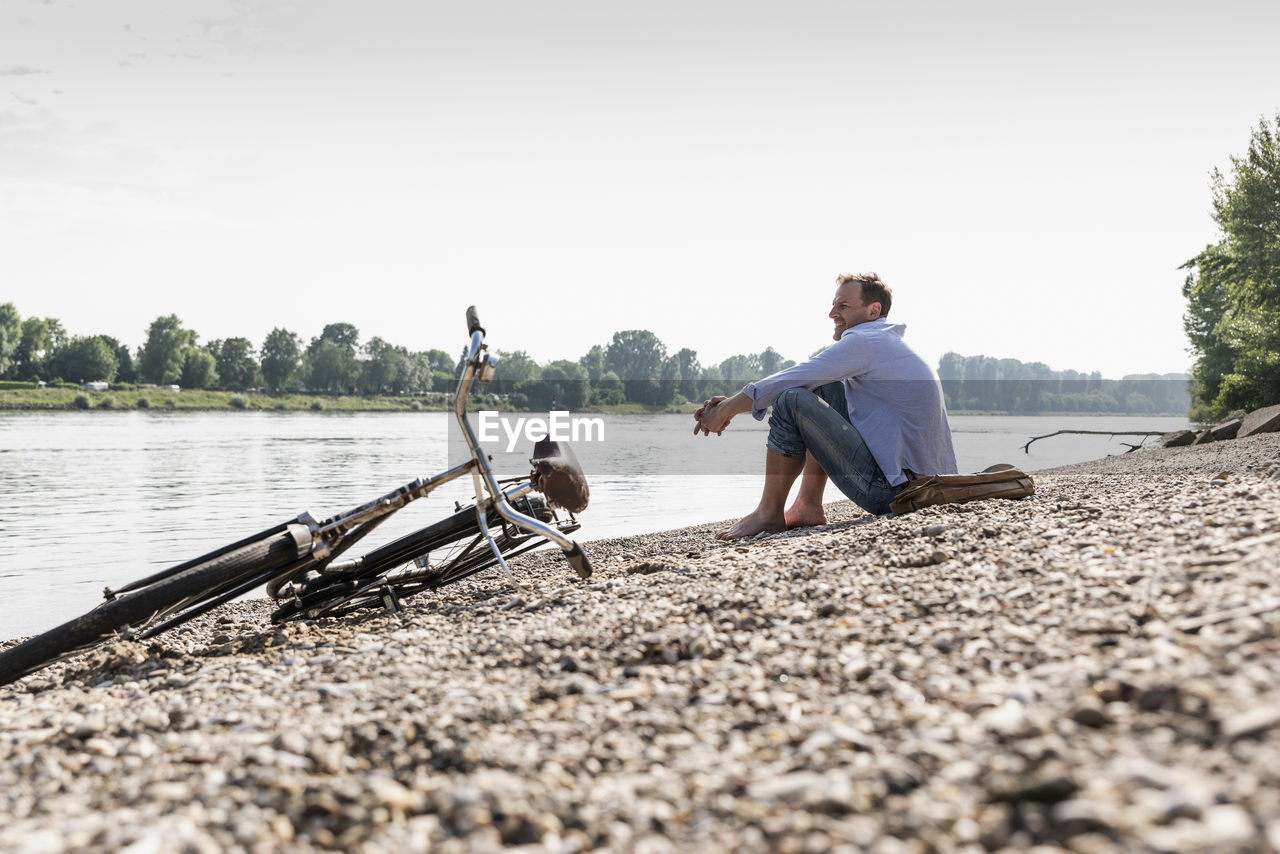 Mature man with bike sitting at rhine riverbank