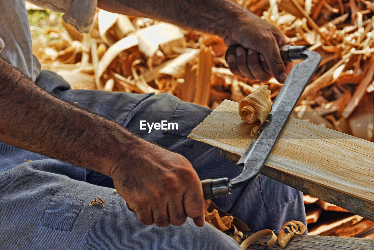 Midsection of man peeling wood at workshop