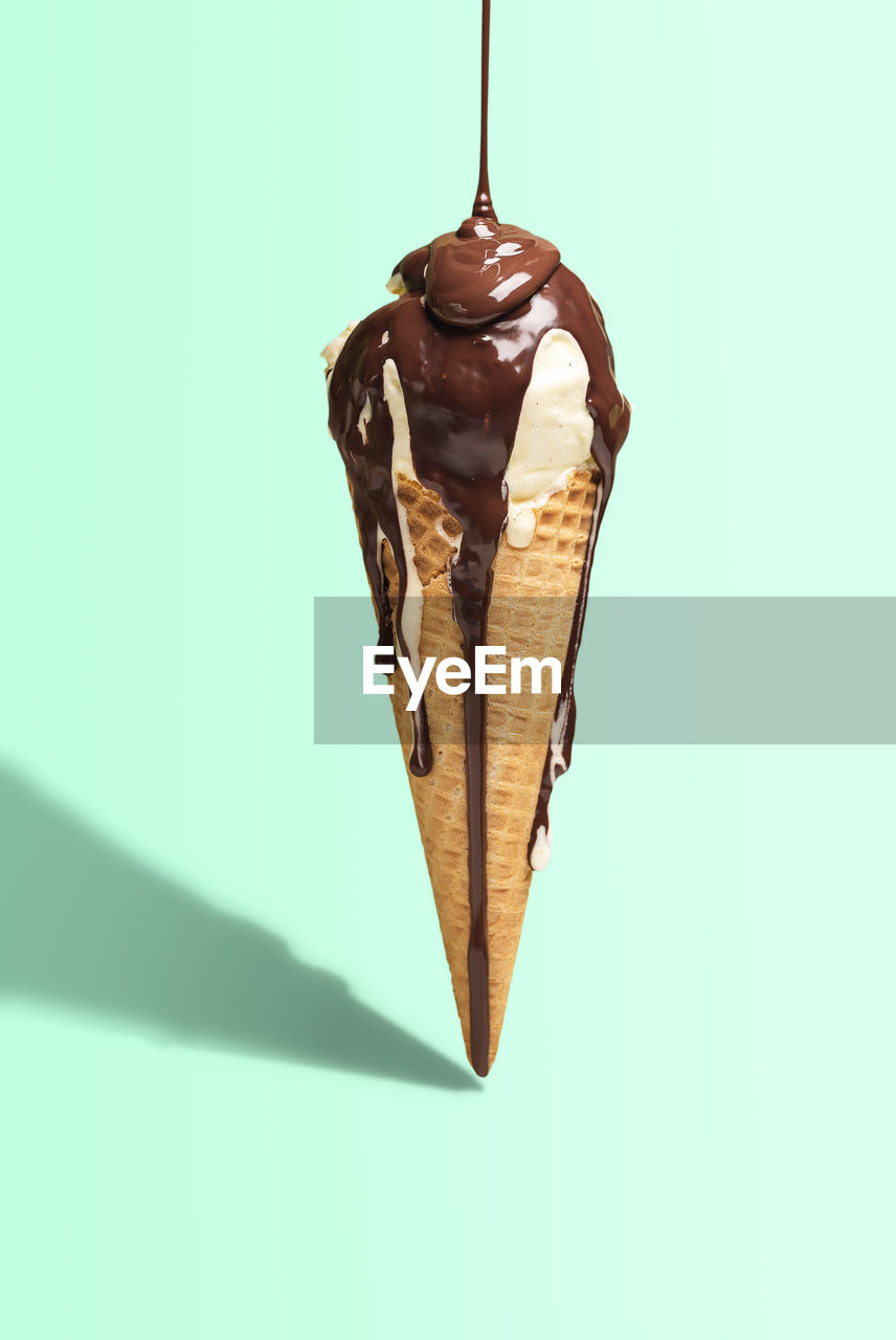 Vanilla ice cream cone with melted chocolate topping on green background harsh light. summer dessert