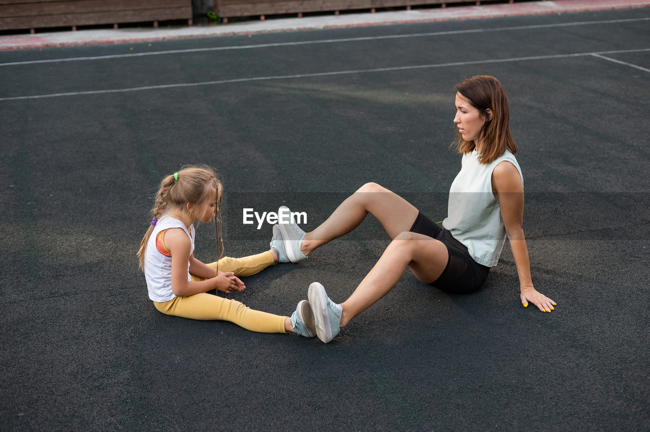 Woman with daughter sitting on footpath