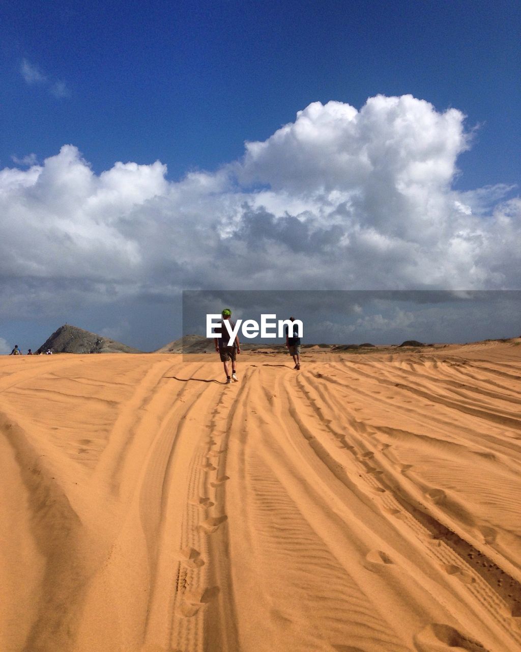 Rear view of men walking in desert against cloudy sky