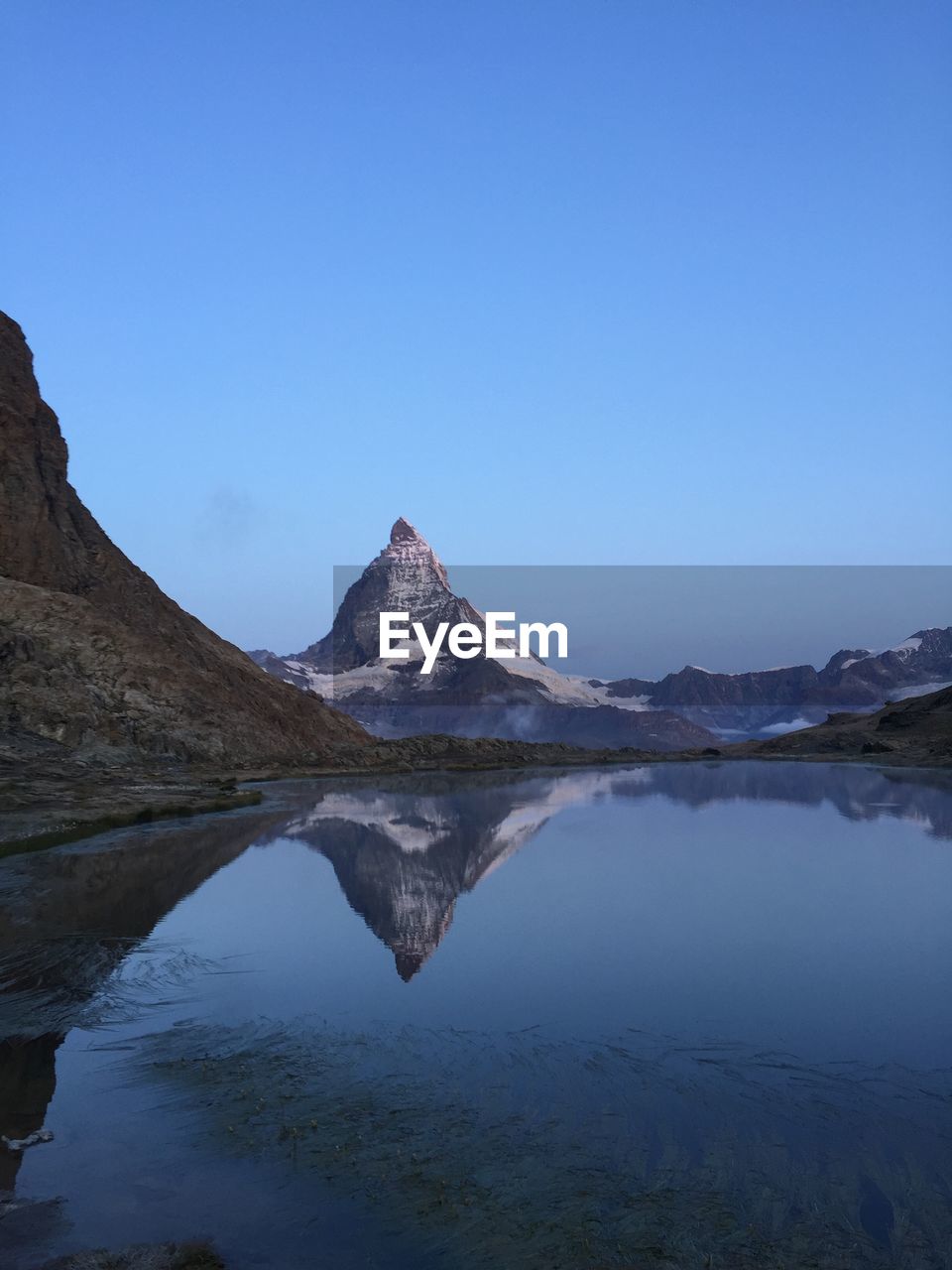 Scenic view of lake and mountains against clear blue sky