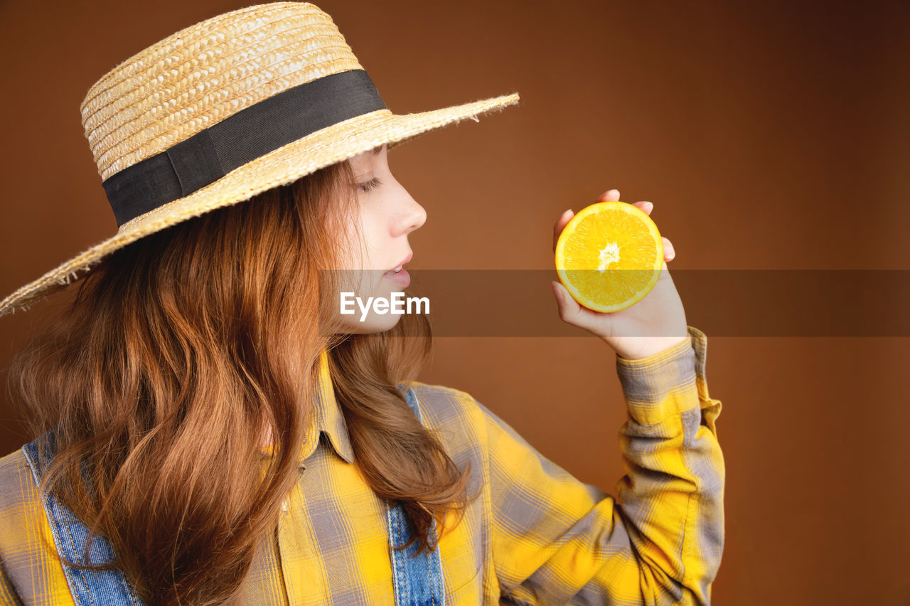Young attractive long-haired caucasian woman holding an orange fruit in her hand and looking at it