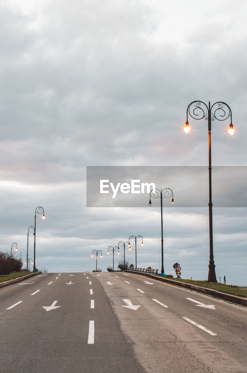 Street lights on road against cloudy sky