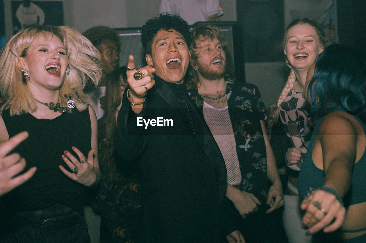 Young non-binary person dancing amidst multiracial friends enjoiying at nightclub