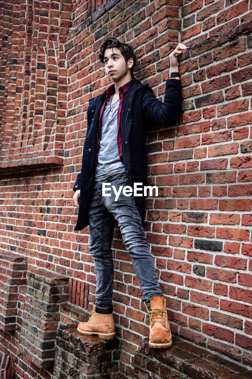 Full length of young man standing against brick wall