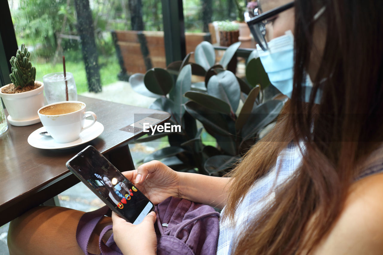 MIDSECTION OF WOMAN HOLDING SMART PHONE AT CAFE