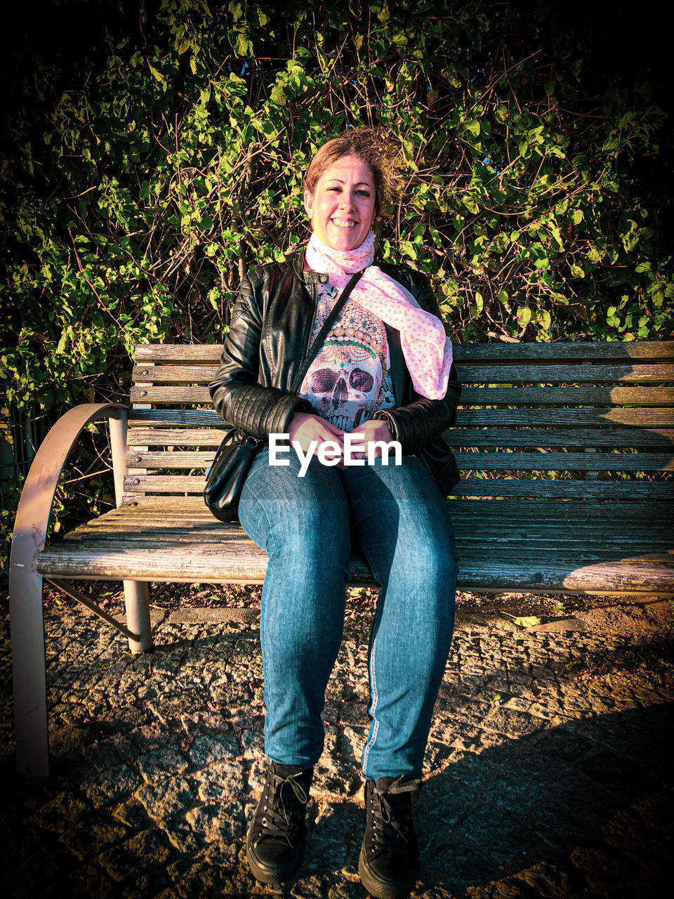 one person, full length, adult, seat, sitting, casual clothing, portrait, bench, front view, looking at camera, jeans, lifestyles, leisure activity, nature, emotion, plant, relaxation, person, furniture, park, footwear, women, clothing, smiling, spring, park - man made space, chair, blue, outdoors, young adult, park bench, men, day, mature adult, happiness, tree