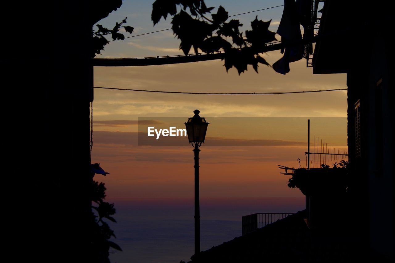 LOW ANGLE VIEW OF ILLUMINATED STREET LIGHT BY SEA AGAINST SKY