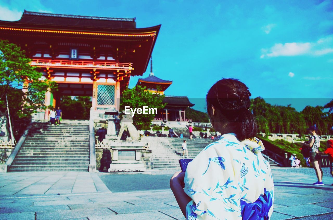 REAR VIEW OF WOMAN OUTSIDE TEMPLE AGAINST BUILDING