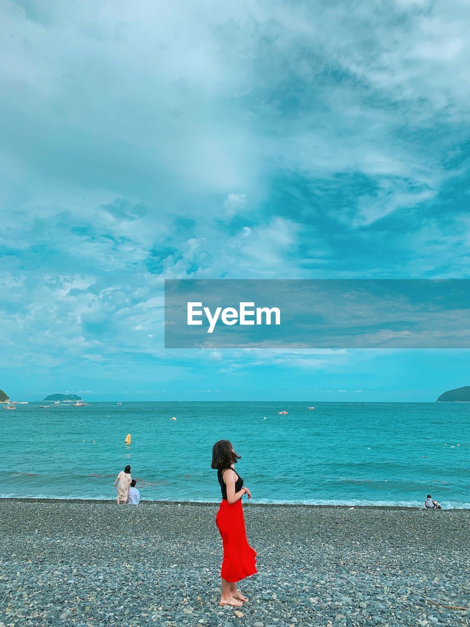 REAR VIEW OF WOMAN STANDING AT BEACH AGAINST SKY