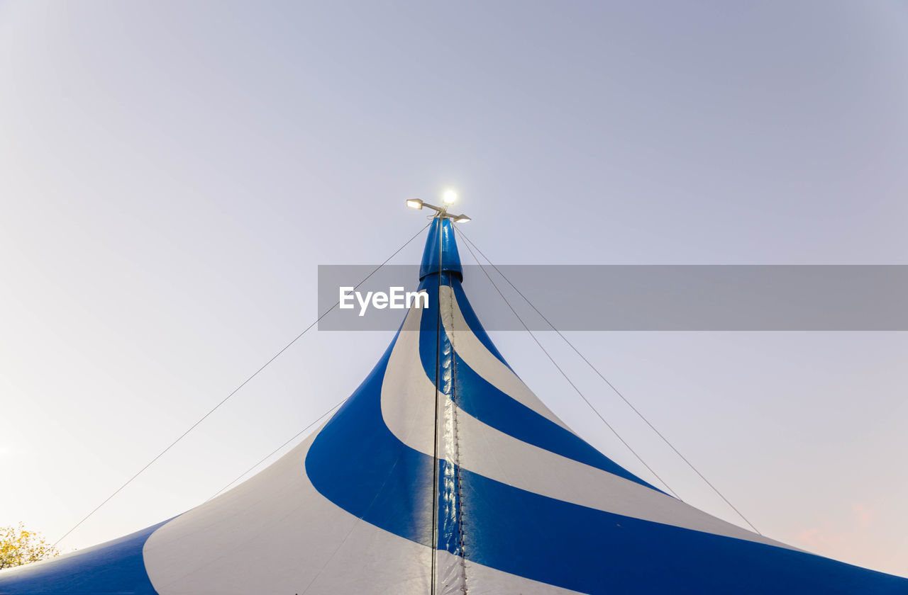 Low angle view of illuminated lights on striped circus tent against sky
