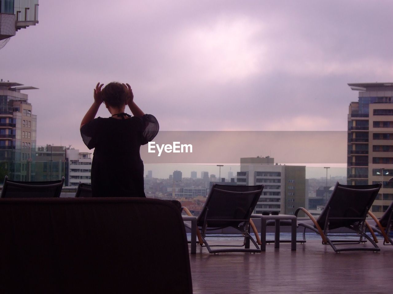 Rear view of woman standing by lounge chairs at poolside on building terrace