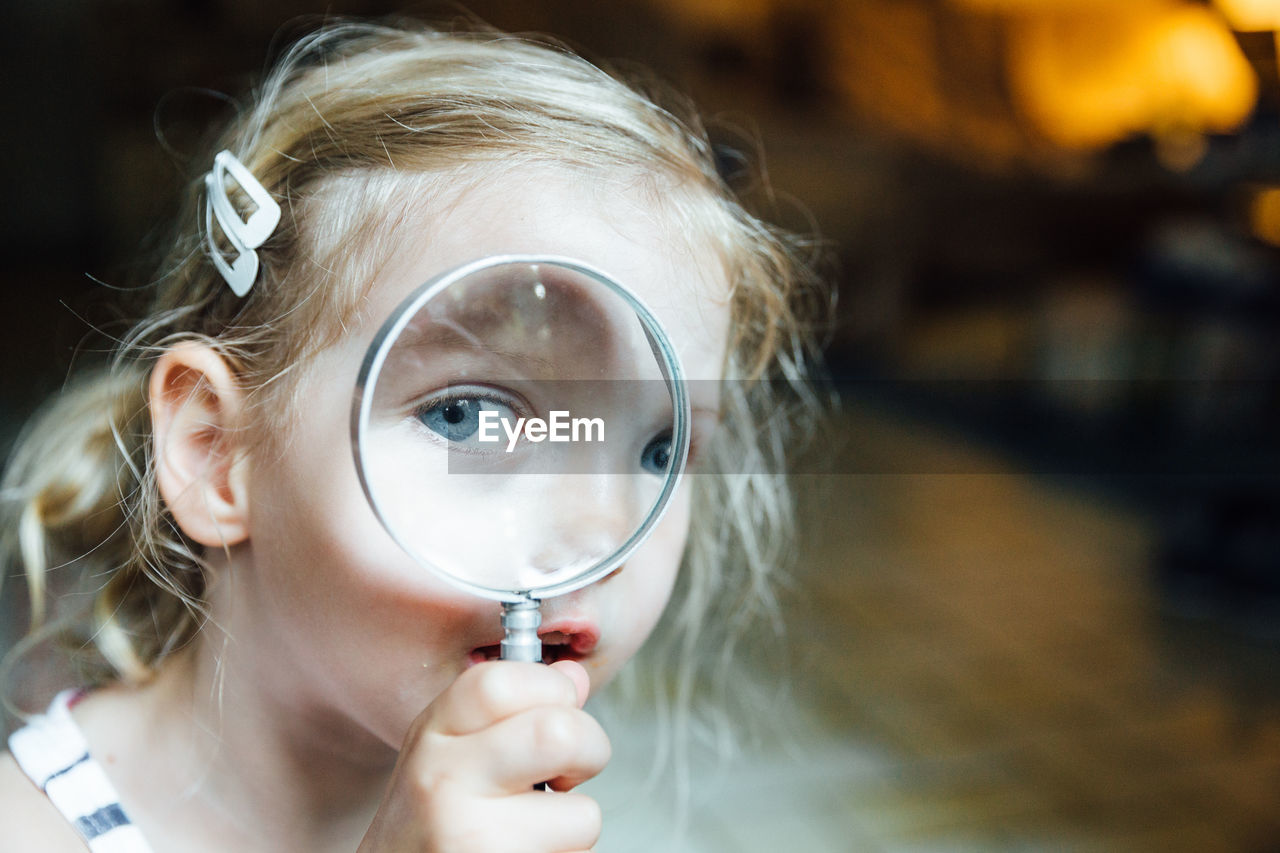 Close-up portrait of girl looking through magnifying glass