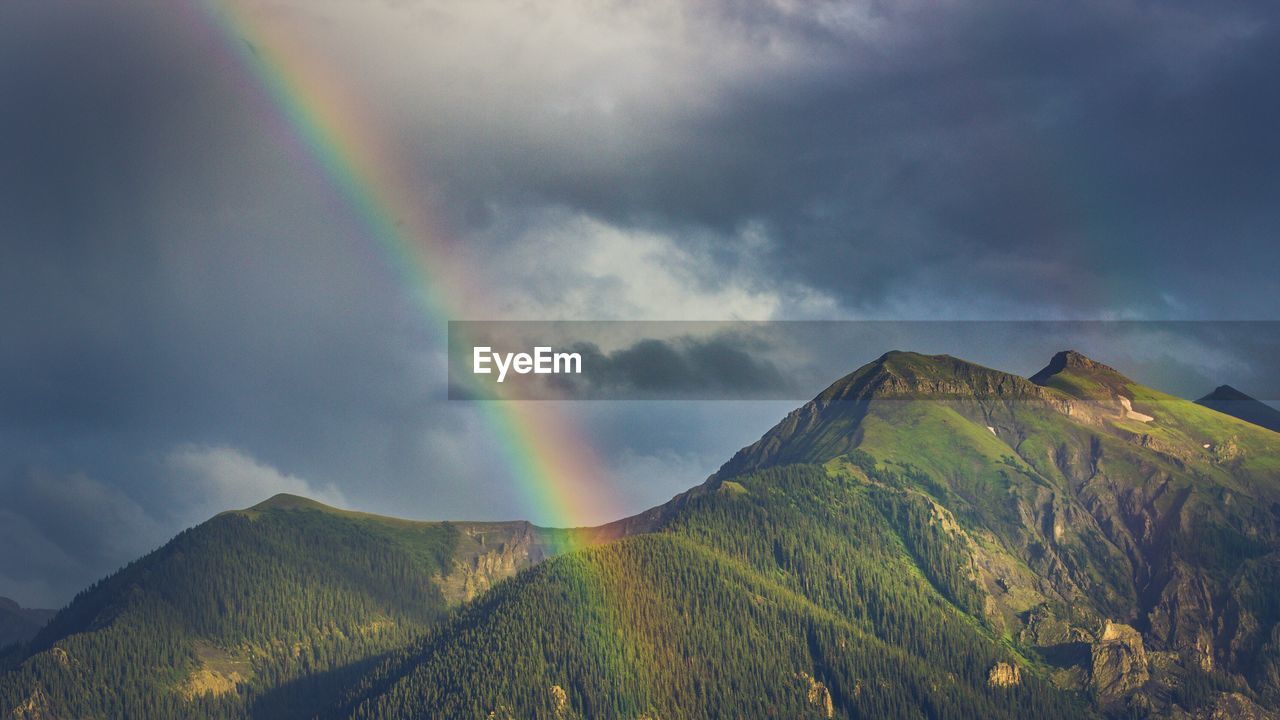 Scenic view of mountains against cloudy sky with rainbow