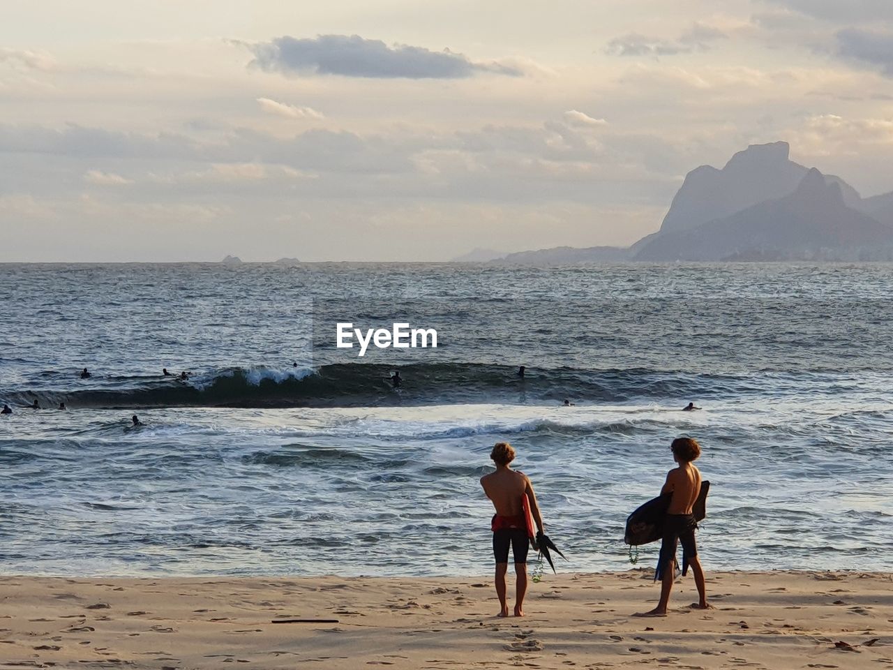 REAR VIEW OF PEOPLE AT BEACH DURING SUNSET