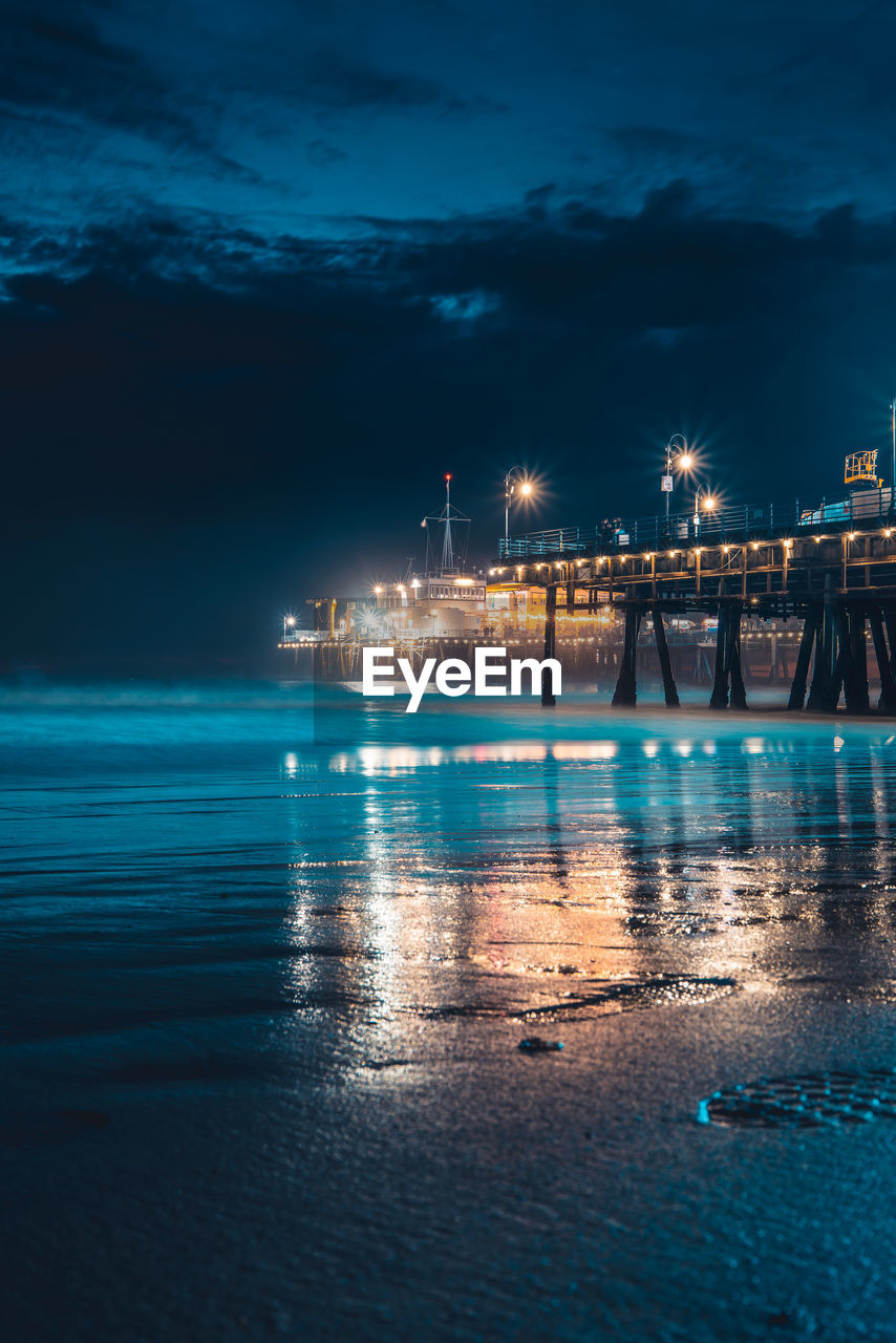 Illuminated city by sea against sky at night