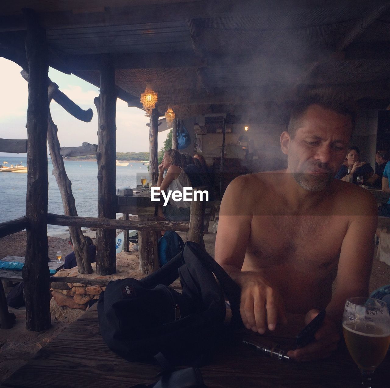 Shirtless man sitting by drink in glass and sea