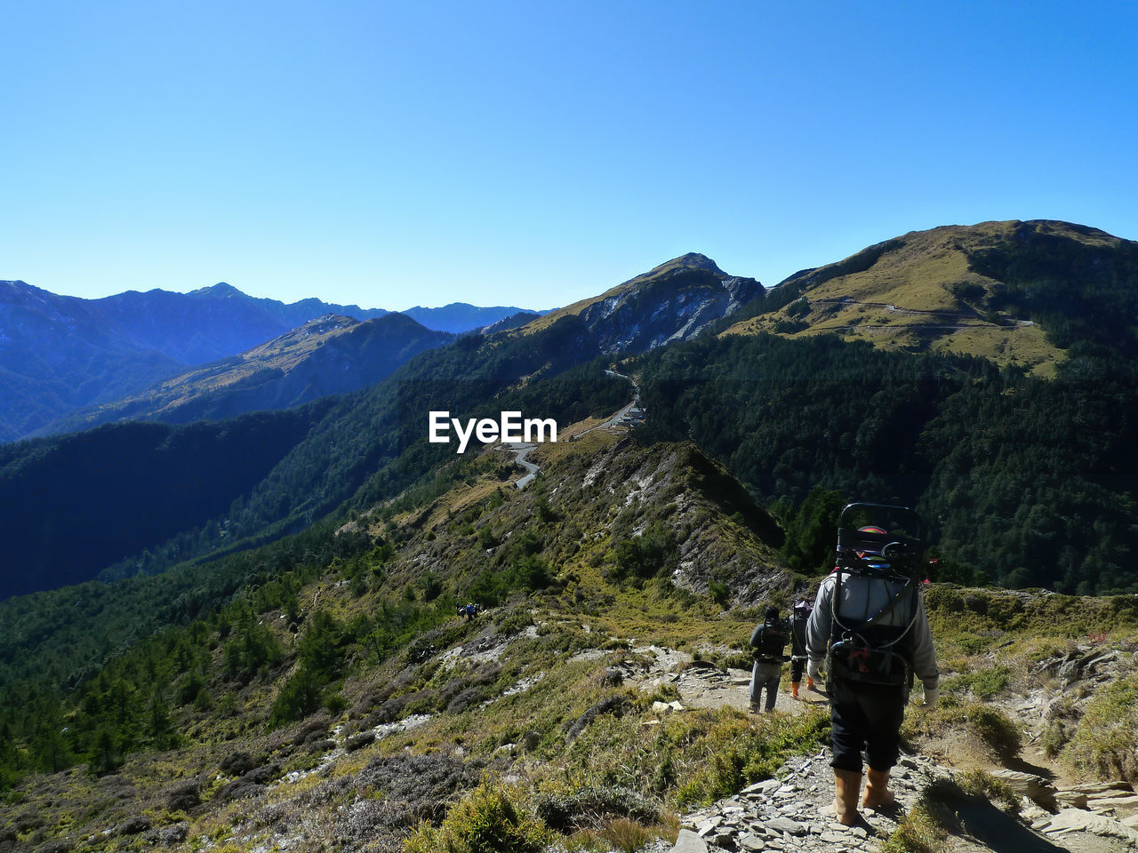 REAR VIEW OF MAN STANDING ON MOUNTAINS AGAINST SKY