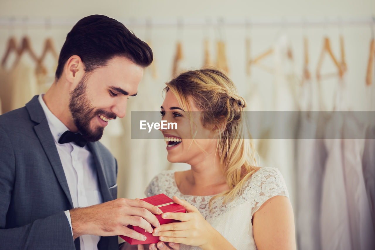 Happy young couple holding gift while standing at bridal shop