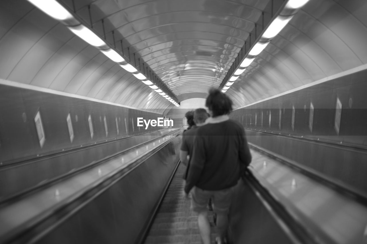 REAR VIEW OF MAN WALKING ON ESCALATOR IN SUBWAY STATION