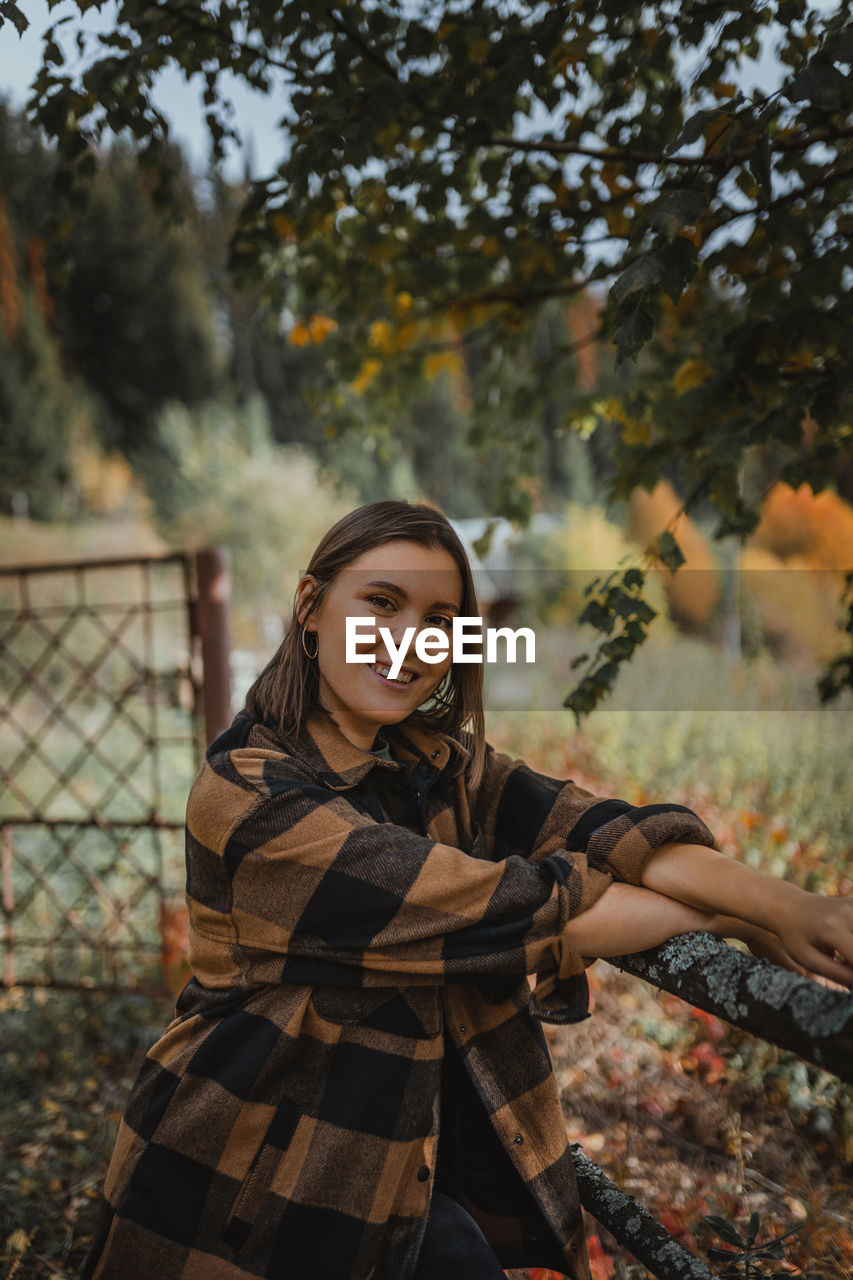 Portrait of smiling young woman standing against fall trees