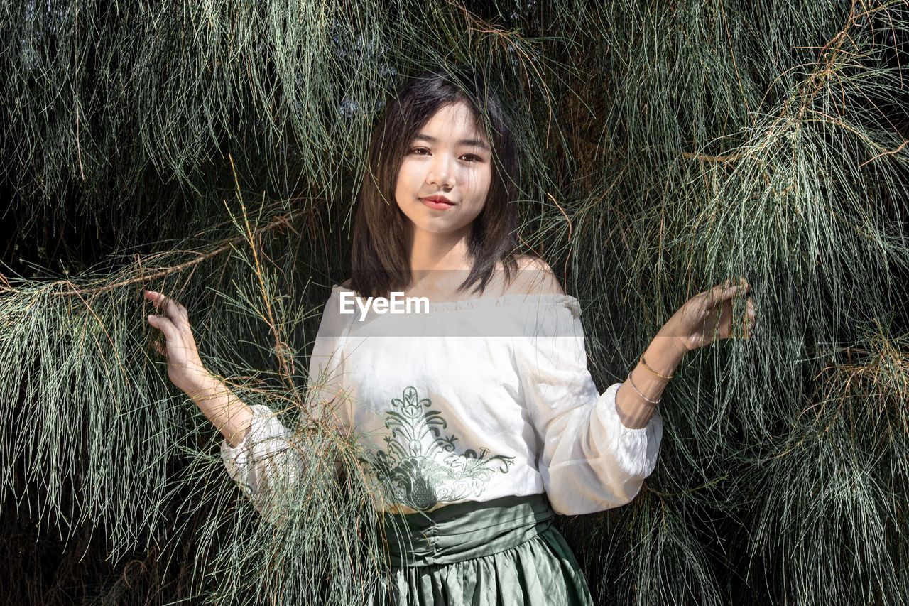 A beautiful girl standing among pine leaves in a pine forest and the dull sunlight.