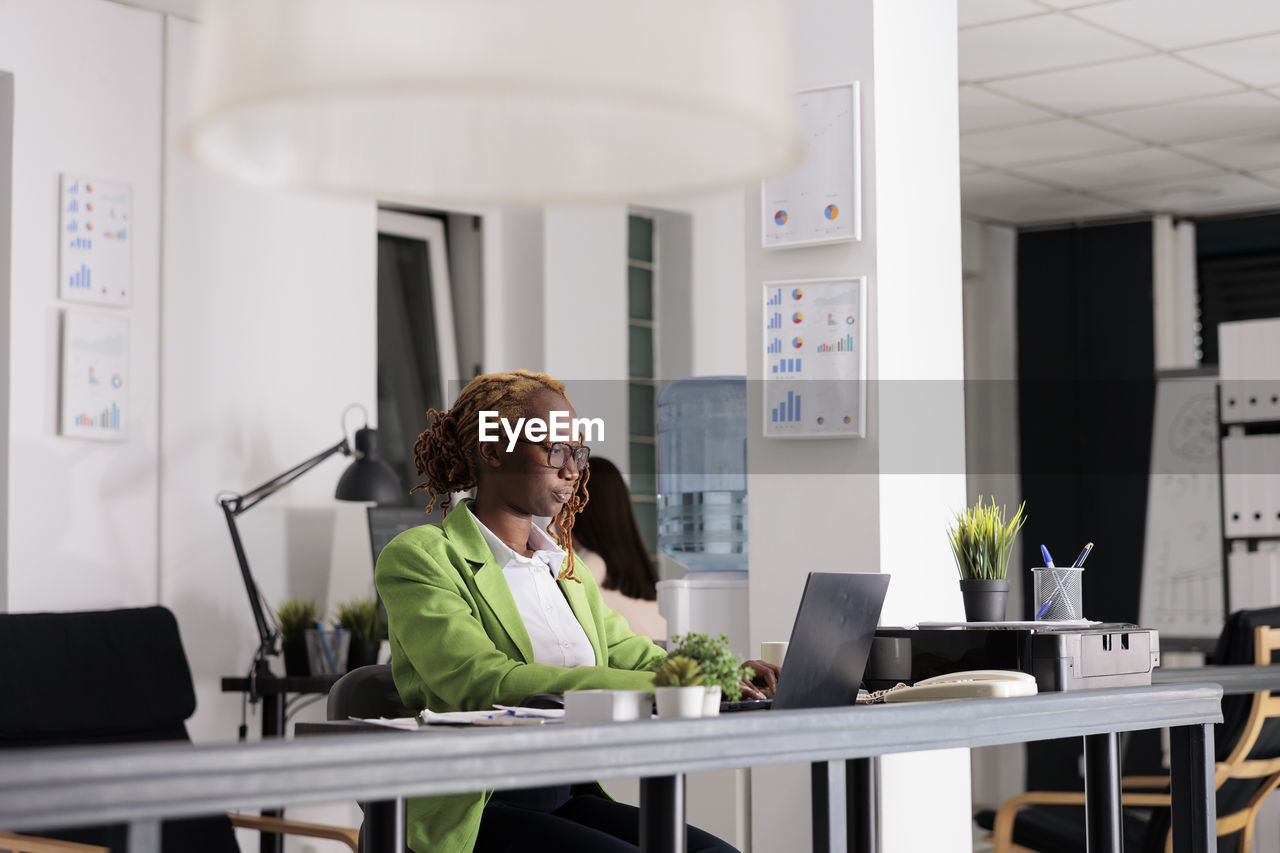 portrait of young woman using laptop at desk in creative office