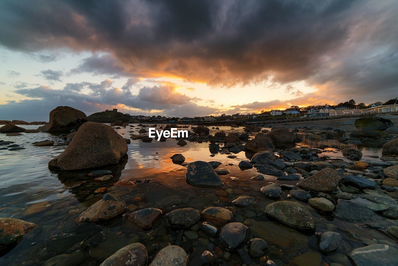 Rocks on shore at beach against sky during sunset