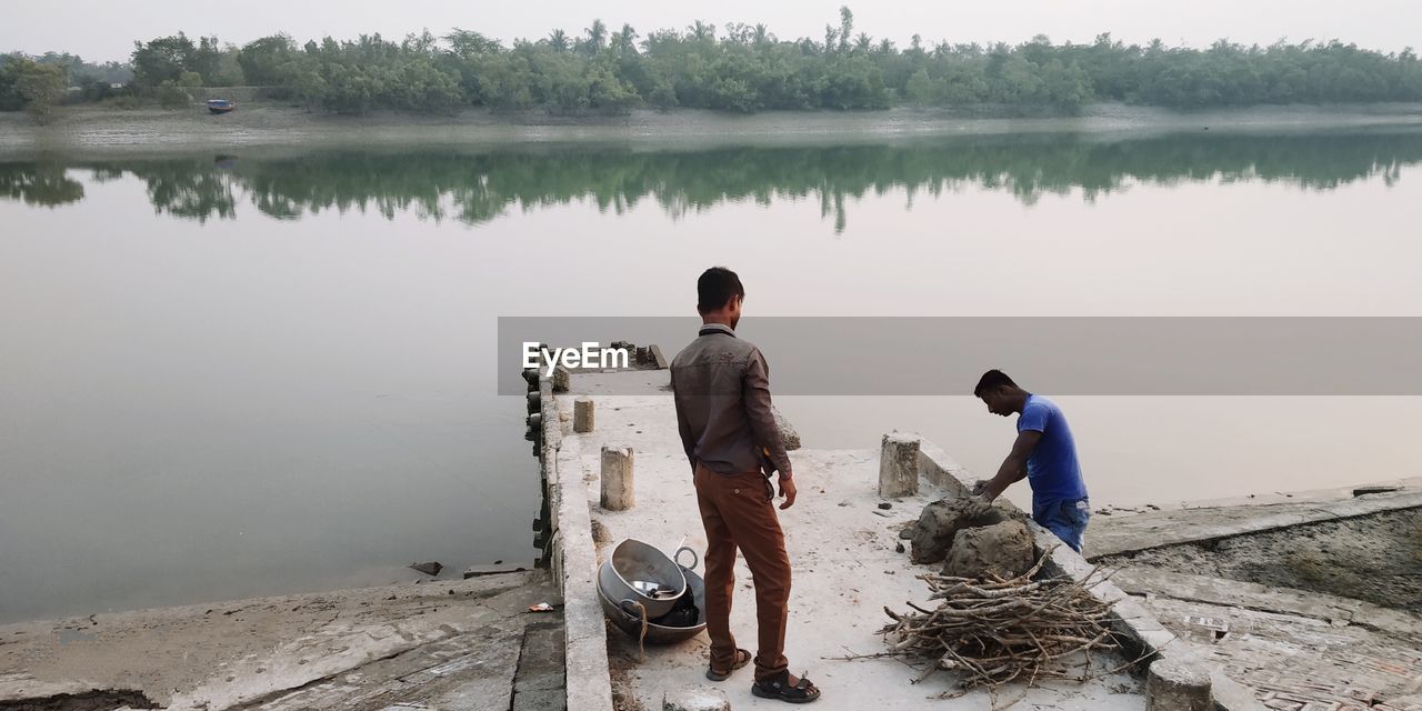 REAR VIEW OF MEN SITTING AT LAKE