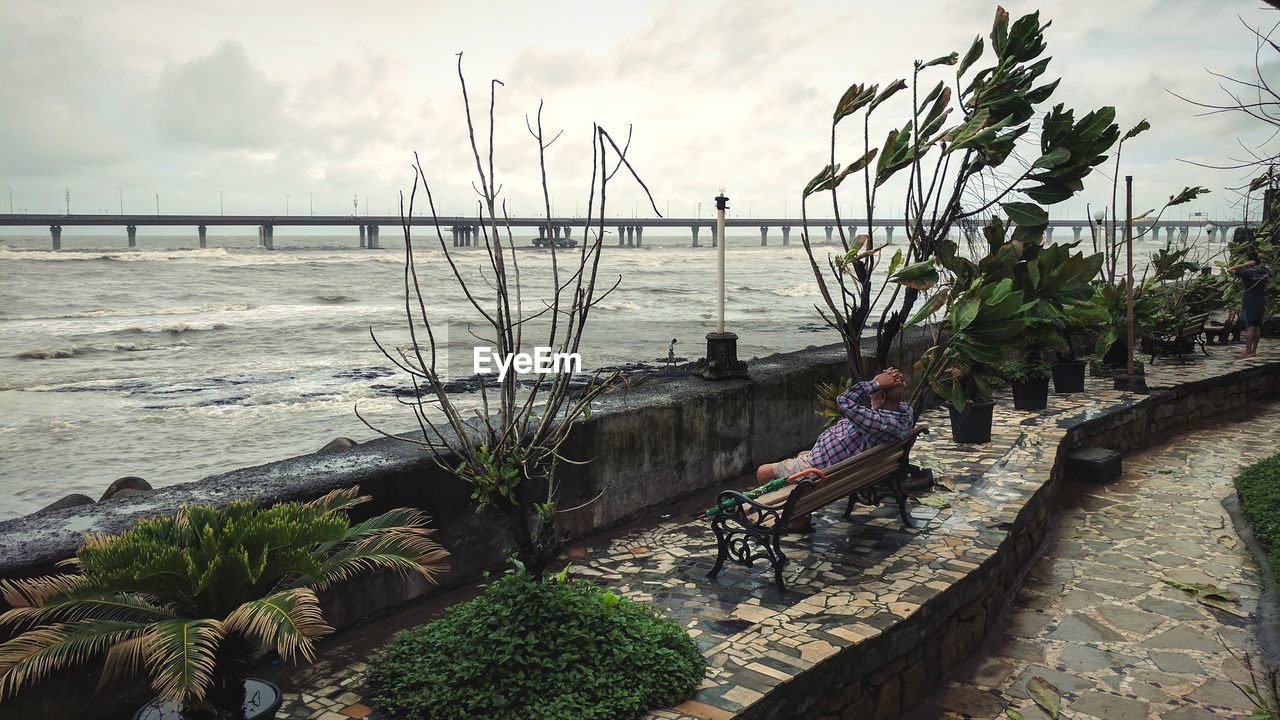 Man sitting on bench against sea