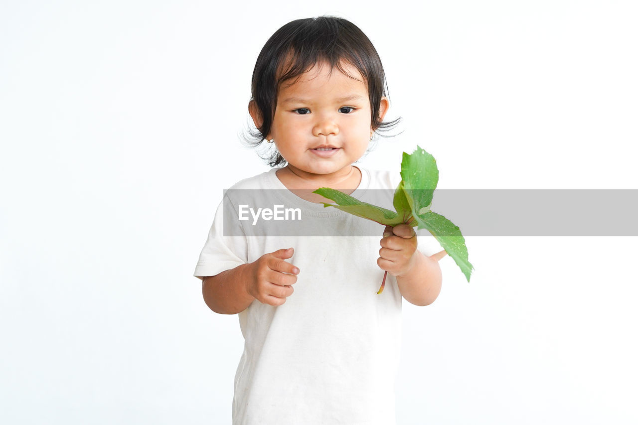 childhood, white background, child, studio shot, one person, cute, portrait, hand, indoors, person, wellbeing, healthy eating, baby, toddler, cut out, human face, food, holding, growth, nose, vegetable, smiling, human head, plant, clothing, arm, finger, food and drink, looking at camera, happiness, leaf, freshness, copy space, plant part, lifestyles, nature, waist up, men, human mouth, white, emotion, female, front view, fun, eating, lap dog, education, culture, innocence, flower, women, human hair, black hair, positive emotion