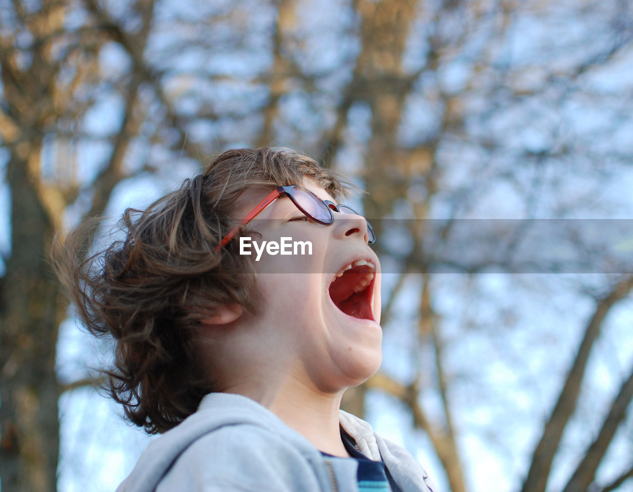 Close-up of boy screaming while standing against bare trees